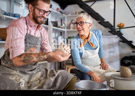 smiling teacher explaining to student how to model a clay pot on workshop. Creative, hobby ,activities concept Stock Photo