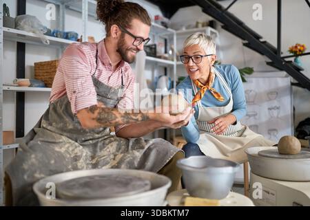 pottery workshop. Happy beginner Making pot from clay while teacher explaining how. Creative, hobby ,activities concept Stock Photo