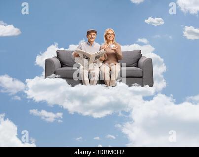 Mature man with a newspaper and woman drinking tea seated on a sofaa floating on a cloud Stock Photo
