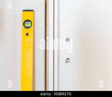Yellow spirit level leaning against wall next to a just installed white door, a construction worker is checking alignment during a house renovation Stock Photo