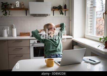 Cheerful middle aged businesswoman leaning back in chair resting arms, feeling satisfied with work done. Relaxed female employee resting from computer screen, looking at window after busy day. || Model released Stock Photo