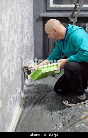 A man applies textured plaster to a wall, showing home improvement and craftsmanship. This demonstrates interior design, renovation, plastering, and t Stock Photo