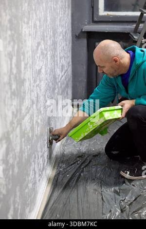 In a captivating close-up, a focused man meticulously applies textured plaster to a wall, showcasing his expertise in home improvement and interior de Stock Photo