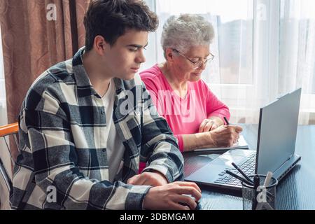 Grandson helping grandmother with computer, teaching digital skills, elderly woman learning technology, family support, intergenerational communicatio Stock Photo