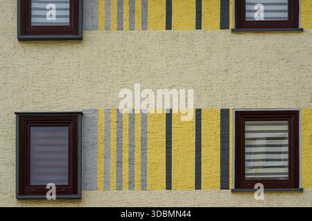 Residential building facade, Hildesheim, Germany, painted in yellow with grey and black vertical stripes, four windows with brown frames, striped blinds inside, Stock Photo