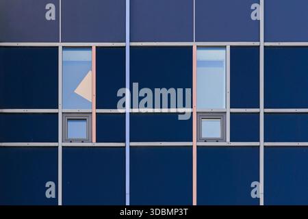 Stockholm, Sweden, Minimalist building facade with a grid of dark blue panels, thin metallic frames, small square windows, two larger rectangular windows, and a triangular shape cutting across one pane Stock Photo