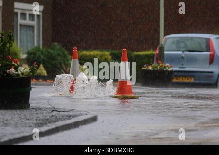 Surface water gushing from road drain during heavy rainfall, drain unable to cope with volume of water causing flooding. Stock Photo