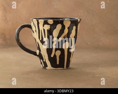 Studio shot of a handmade black ceramic mug with abstract cream glaze pattern on a neutral background. Artisanal pottery object showcasing craftsmansh Stock Photo