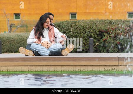 Multiehnic couple sitting together by fountain enjoying playful moment outdoors Stock Photo