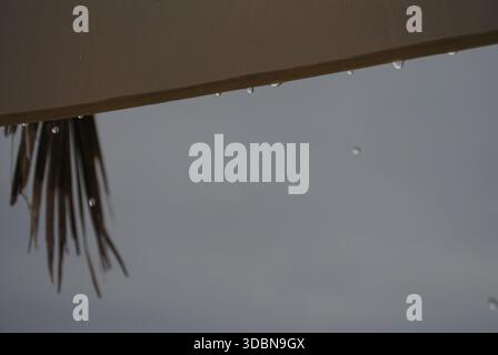 Raindrops are falling from the wet sunshade under the cloudy grey sky at bora time on the Adriatic sea Stock Photo