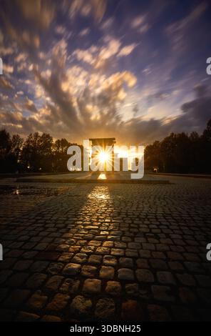 Golden sunrise shining through the Temple of Debod in Madrid, with dramatic clouds and reflections on wet cobblestones. Stock Photo