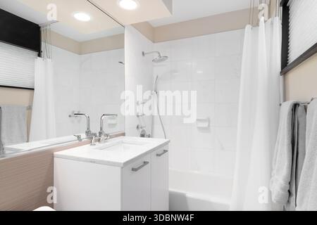 A clean and modern brown bathroom featuring a white vanity and sink, bathtub, and shower with a white curtain and white square tiles. Stock Photo