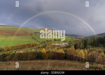 Autumn colors fill rolling hills with a village, rainbow arches over fields and trees. Stock Photo