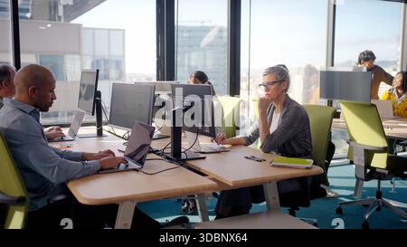 Middle aged businesswoman working at open plan office desk Stock Photo