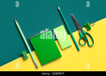 Top view of spiral notepad and school supplies over yellow and green background Stock Photo
