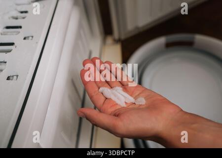 Male hand holding chunk of ice extracted from freezer during defrosting process, with melting ice pooling in containers positioned below. Stock Photo