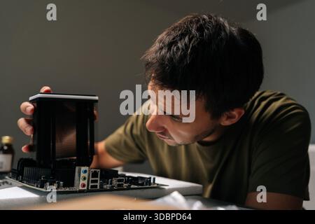 Close-up of concentrated computer technician male carefully installing CPU cooler onto motherboard, performing maintenance and upgrade service on Stock Photo