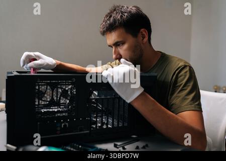 Focused computer technician in protective white gloves carefully installing internal hardware components inside open desktop computer case Stock Photo