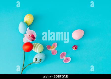 Spring composition with colored Easter eggs and flowers on pastel blue background. Minimal Easter concept. Creative festive holiday layout. Stock Photo