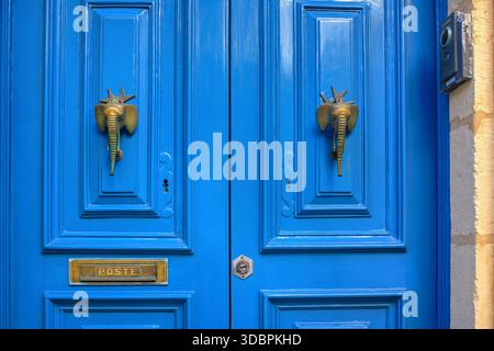 Traditional bright blue Mediterranean wooden door in Sliema, Malta, featuring ornate brass elephant-head door knockers and a vintage POSTE mail slot. Stock Photo