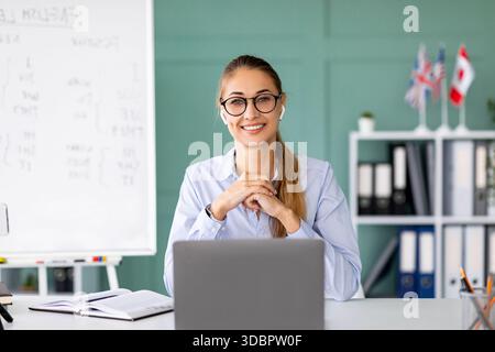 Happy English Teacher Engaging Students in an Online Lesson Near a Blackboard With Grammar Rules Stock Photo