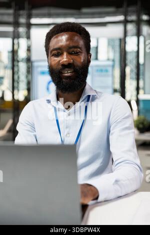 African American male employee working at modern office workspace, reading emails on digital device. Portrait of black man analyzing company data on laptop, and reviewing online reports. Stock Photo