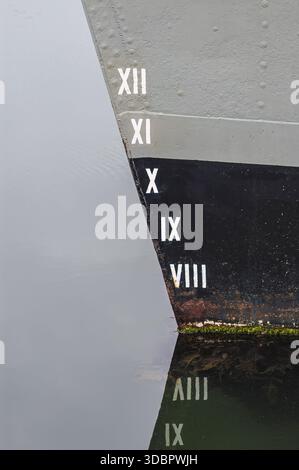 Close-up of a ship’s bow with Roman numeral depth markings from VIII to XII along the hull, reflected in the calm water Stock Photo