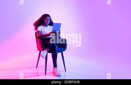 Cheerful Young Black Lady Enjoying Online Study in Neon Light Environment Stock Photo