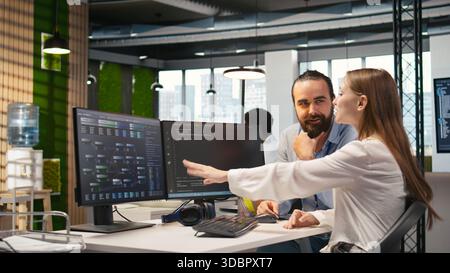 Friendly team leader helping happy young engineer code AI algorithms to debug software issues and improving system stability. Helpful manager assisting smiling intern in tech startup office, camera A Stock Photo