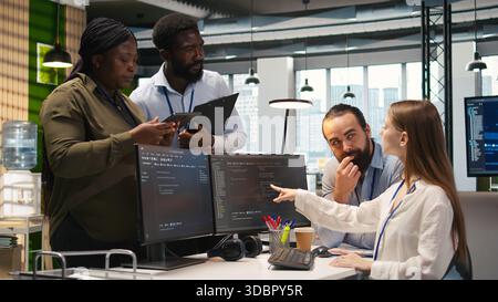 Teamworking programmers developing software applications, working together to optimize code. Tech startup team doing brainstorming in office, using AI to solve bottlenecks, camera A Stock Photo