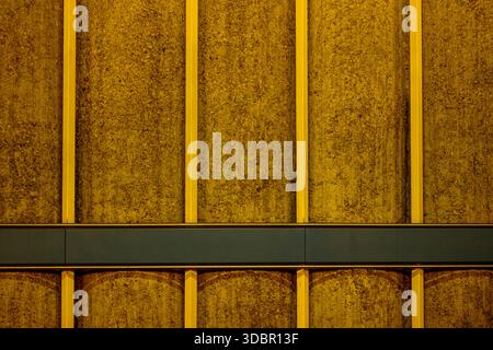 A textured concrete facade illuminated by yellow light in Munich, Germany. The wall is divided by vertical yellow beams and a horizontal blue-gray band. [M] Stock Photo