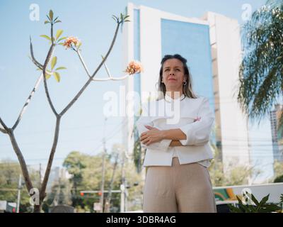 Professional woman posing with crossed arms in front of a tall modern building. Stock Photo
