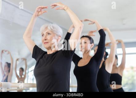 Girls in ballet class perform fifth position with participation of mature female mentor Stock Photo