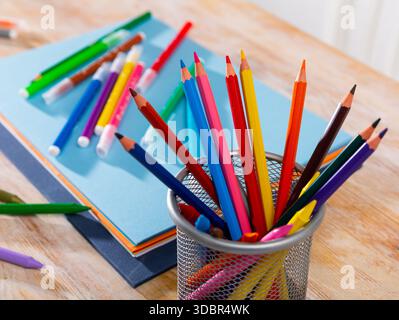 Multicolored wooden pencils on desk with papers and notebooks Stock Photo