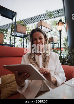 Woman holding a tablet and smiling while seated in a cafe. Stock Photo