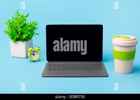 Blank screen computer tablet with keyboard case, desktop with coffee cup, potted plant, alarm clock Stock Photo