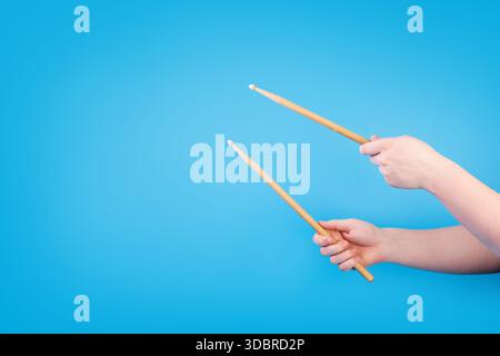 Close up male hands holding drumsticks on an isolated blue background. Concept of drumming lessons, online courses and learning at home. Favourite hob Stock Photo