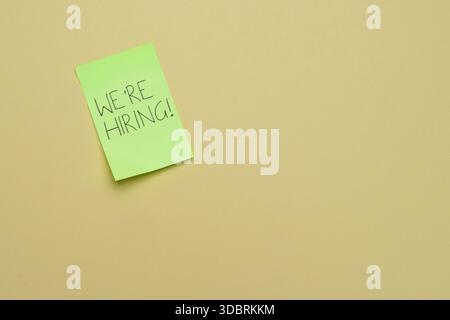 A green sticky note with the handwritten message WE'RE HIRING! on a plain background. Job openings, recruitment, talent acquisition, and employment Stock Photo