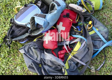 Red emergency first aid kit medical bag with white cross and blue paragliding harness backpack equipment lying green grass field preparing for adventu Stock Photo