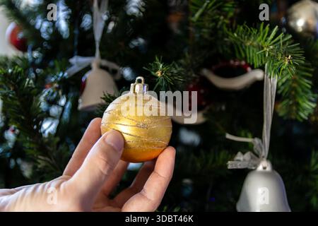 Hand Holding Golden Christmas Ornament on Decorated Tree Stock Photo
