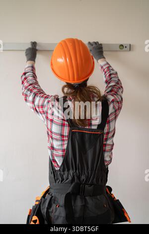 Rear view of Contractor, handyman, builder in uniform measuring wall using bubble spirit level. home renovation and construction concept. Stock Photo