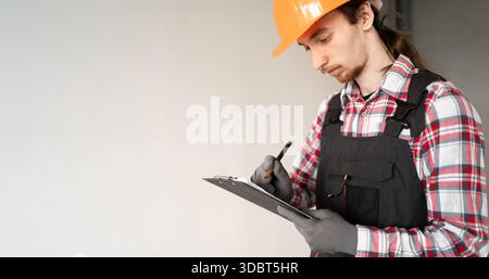 Young male builder writing notes on clipboard at construction site. copy space. banner Stock Photo