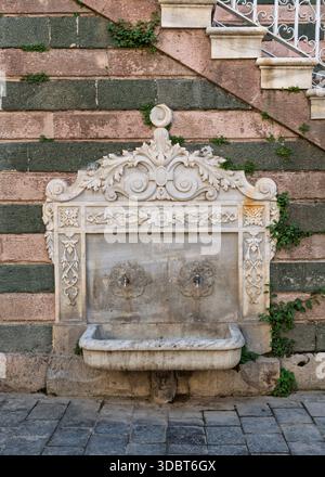 Ornate marble fountain with two spigots and basin on the stone wall of Salepcioglu Mosque, Izmir, Turkey. Historic architecture featuring carved details and natural stone blocks Stock Photo