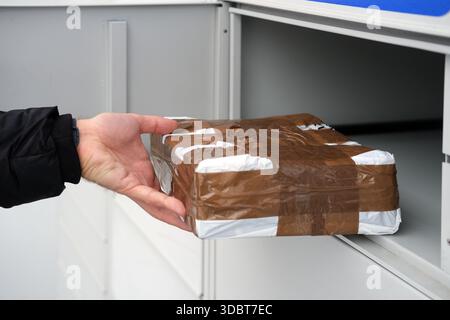 Close-up of a taped cardboard parcel fully removed from a grey metal locker and held in one hand, photographed straight-on with soft daylight Stock Photo