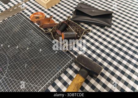 Leather crafting tools and handmade goods on a checkered workbench. High quality photo Stock Photo