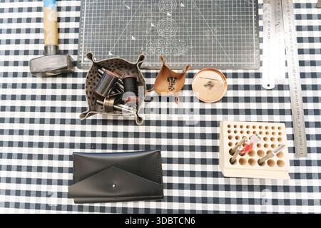 Leather crafting tools and handmade goods on a checkered workbench. High quality photo Stock Photo