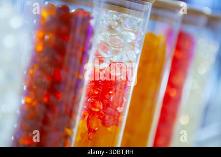 A vibrant, close-up photograph of several clear glass test tubes filled with colorful gelatinous capsules in shades of red, orange, and clear white Stock Photo
