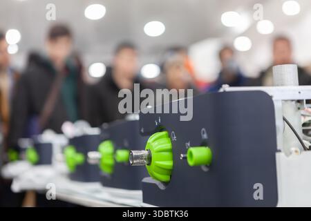 Close-up of advanced green mechanical device at tech exhibition. People observe innovative machinery in the background, showcasing technological... Stock Photo