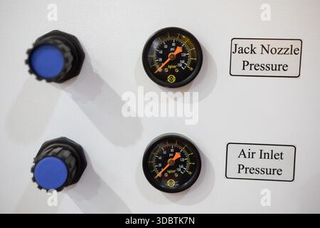 A close-up of a white control panel featuring two pressure gauges for Jack Nozzle and Air Inlet, positioned next to blue adjustment knobs Stock Photo