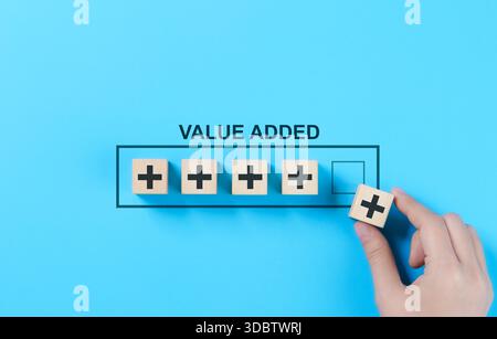 Value Added Concept. A hand arranging wooden blocks with plus signs Value Added representing growth, improvement, and added value in business and proj Stock Photo